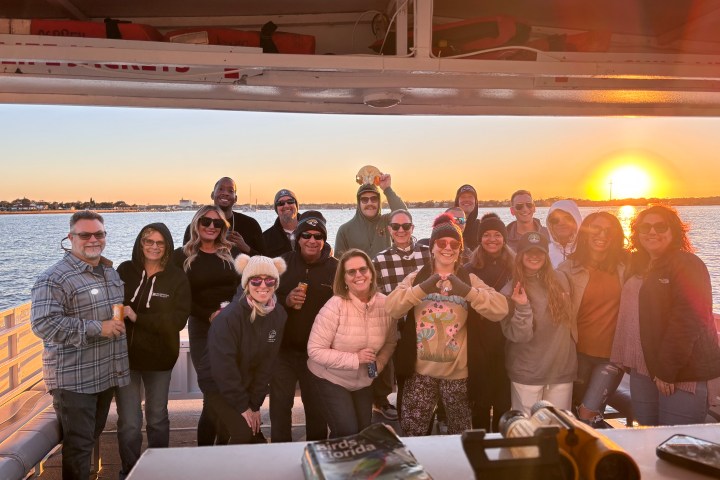 Group of people on a boat at sunset, smiling and posing for the photo.