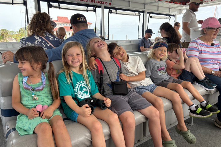 Children sitting closely and smiling on a boat, surrounded by adults.