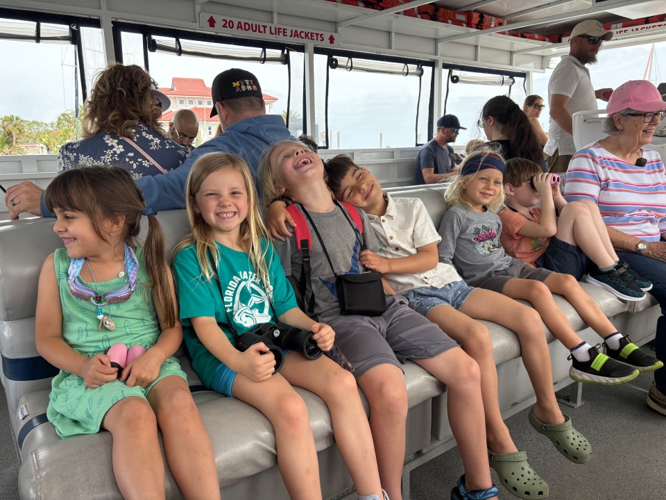 Children sitting closely and smiling on a boat, surrounded by adults.