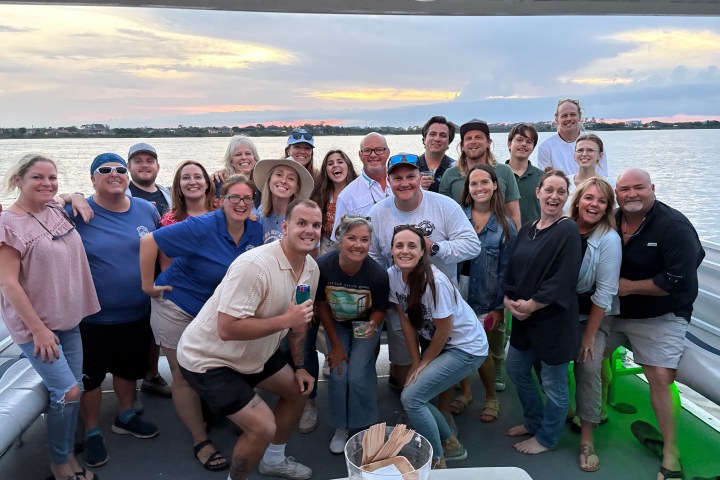 Group of people smiling on a boat at sunset.