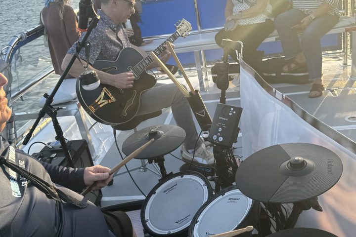 Band playing instruments on a boat at sunset near a city skyline.