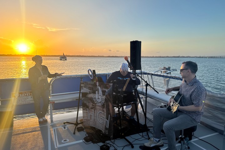 Musicians on a boat at sunset with guitars and a keyboard.