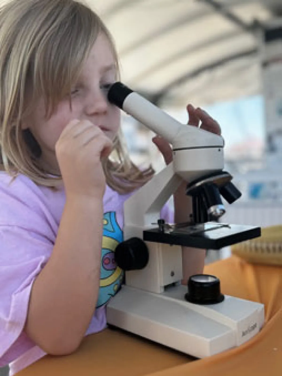 a little girl sitting at a table with microscope