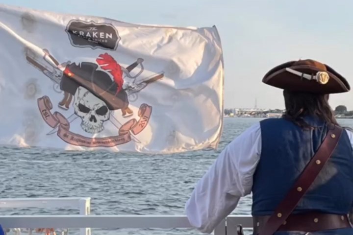 Person in pirate costume on a boat with a pirate flag and safety sign.