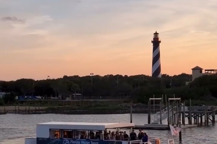 Tour boat on water near a lighthouse at sunset.