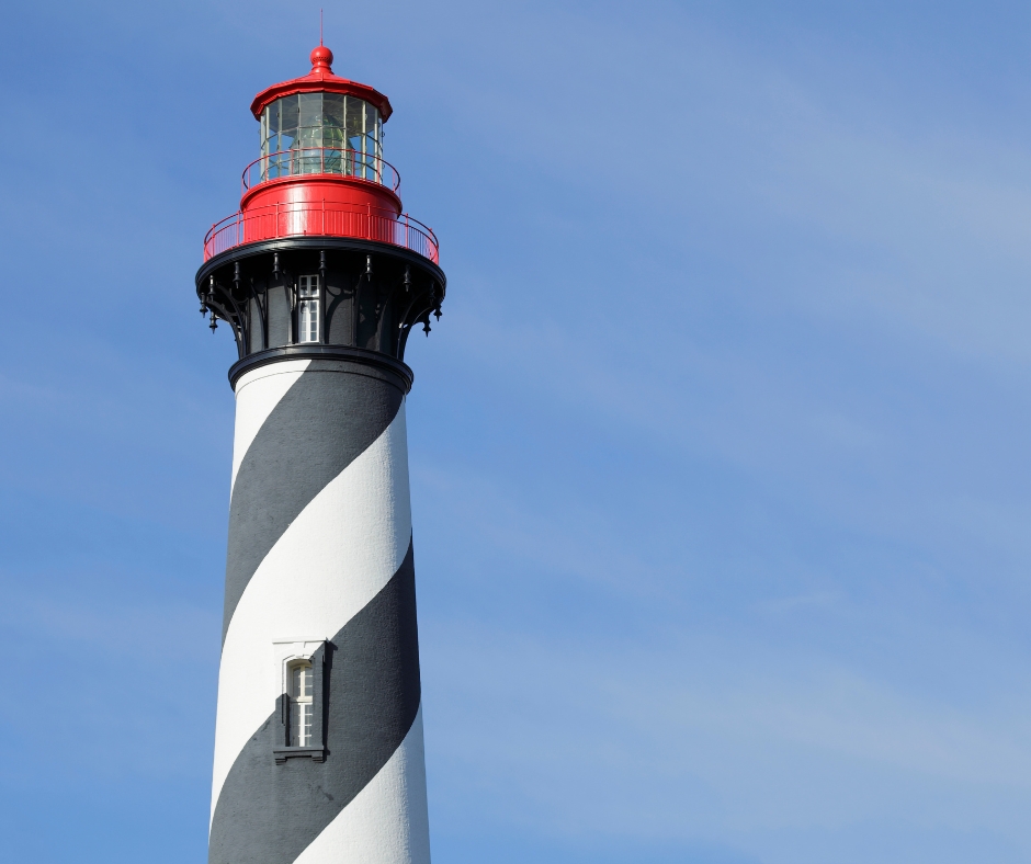 Lighthouse with black and white spiral stripes, red top against clear blue sky.