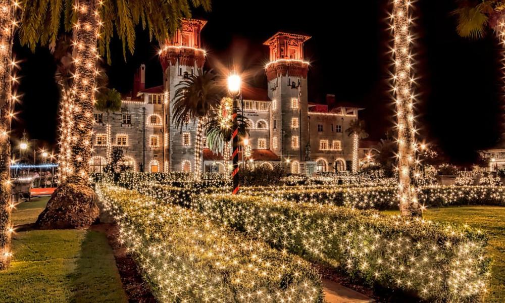 A large building decorated with festive holiday lights at night, surrounded by illuminated palm trees.