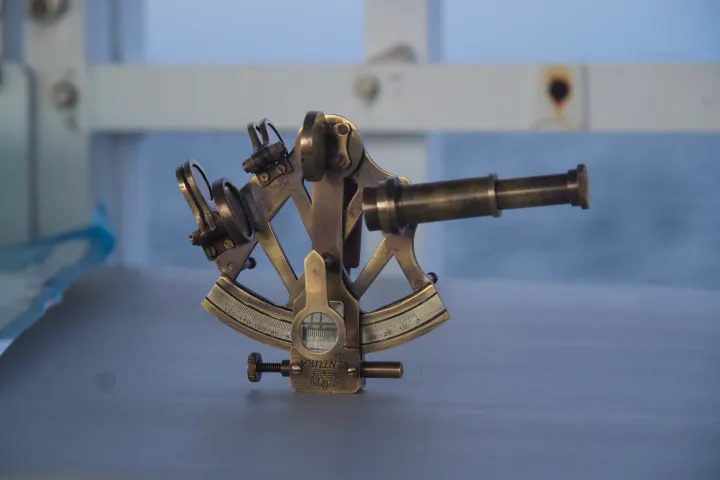 Brass sextant on a table with an ocean background.