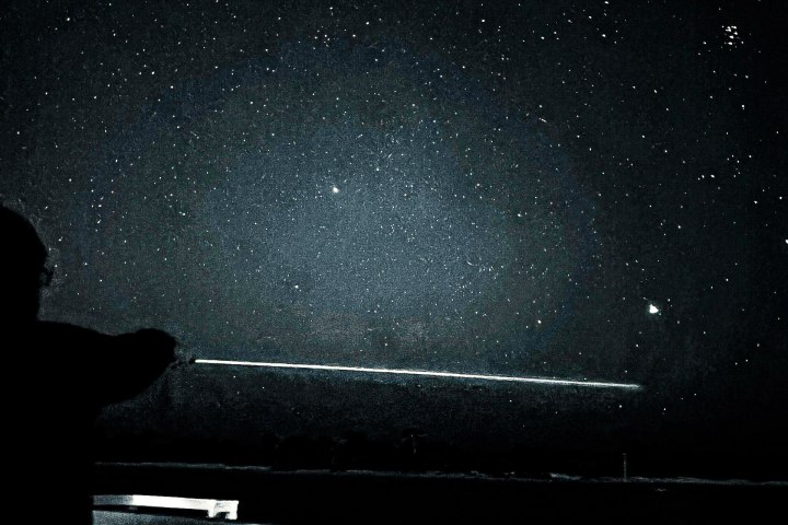Person on deck pointing at starry night sky with a railing in view.