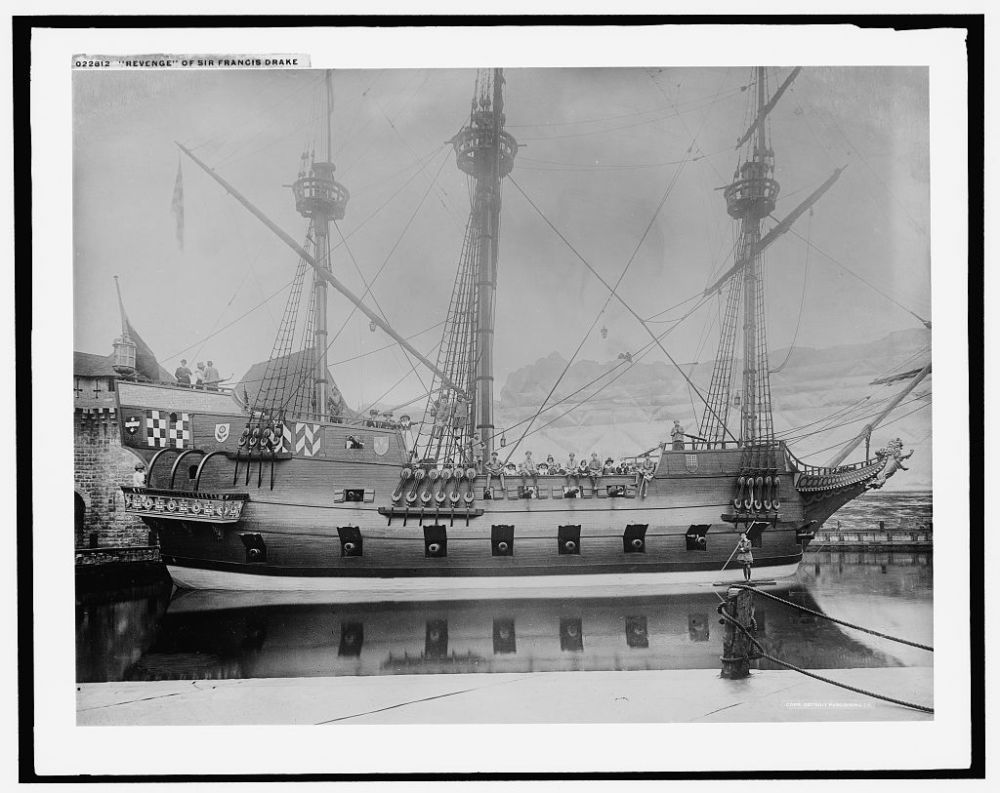 Historic ship 'Revenge' with cannons docked near a stone fort, tall masts and riggings visible.