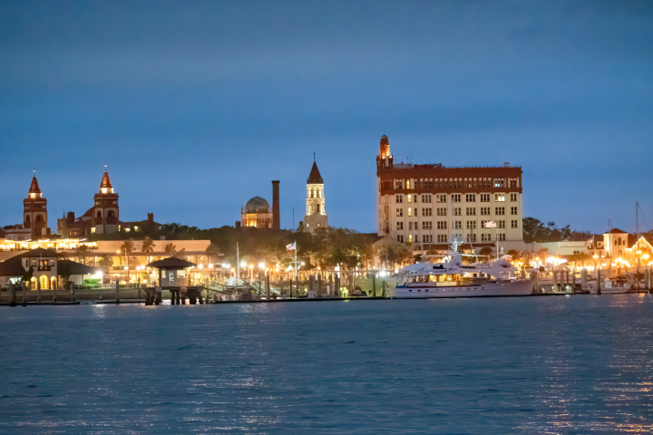 Night view of a waterfront cityscape with lit buildings and docked boats.
