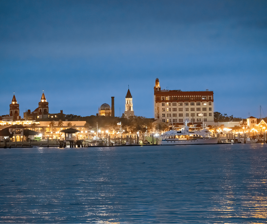 Night view of a waterfront cityscape with lit buildings and docked boats.