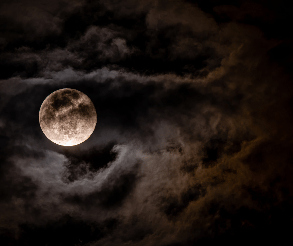 Full moon shining through dark, swirling clouds at night.