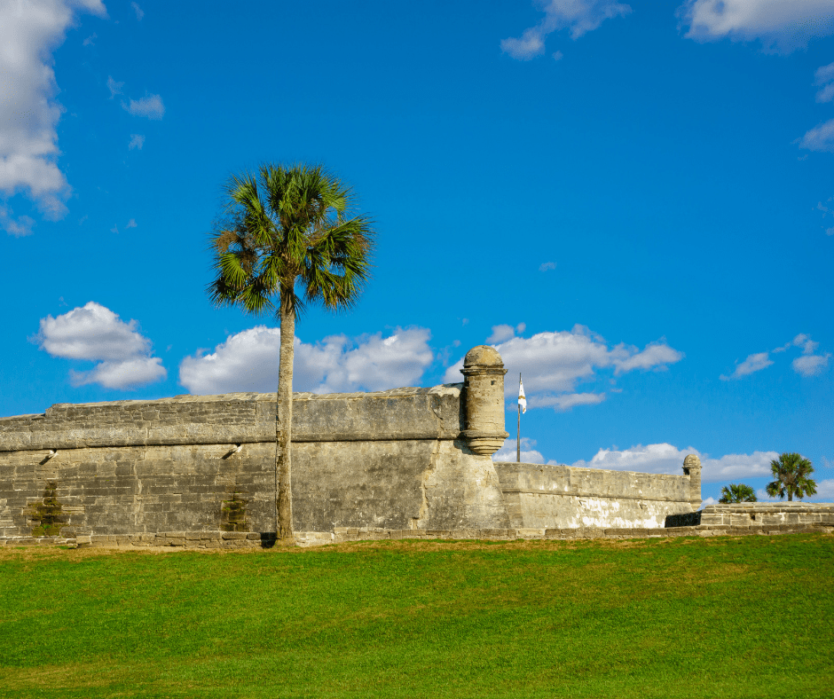 Stone fort with palm tree on grassy area, blue sky background with clouds.