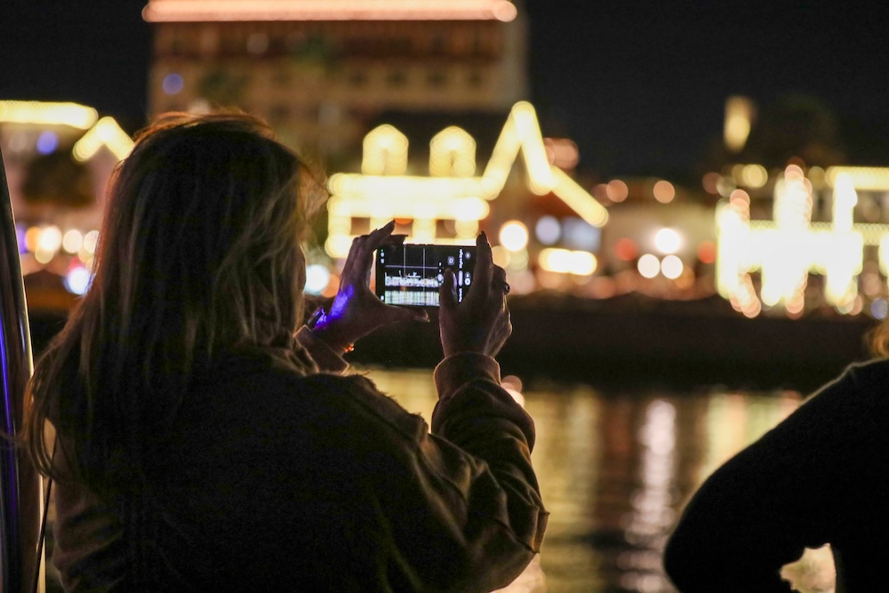 Person taking photo of illuminated buildings at night over water.