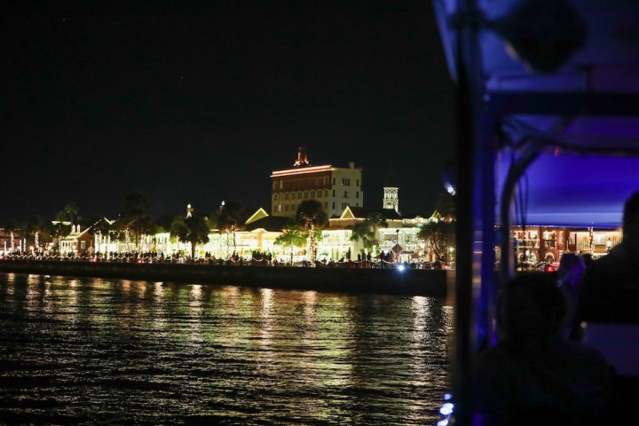 Night view of illuminated buildings along a waterfront, seen from a boat.