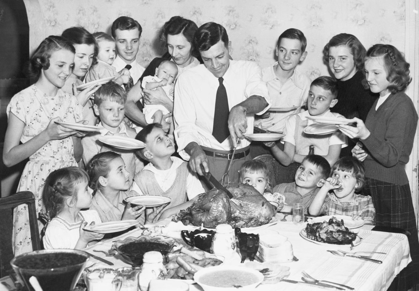 Large family gathered around a dining table as a man carves a turkey.