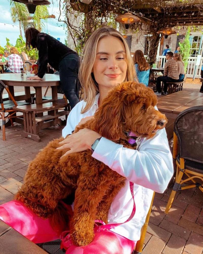 Person sitting outdoors holding a brown fluffy dog on their lap.