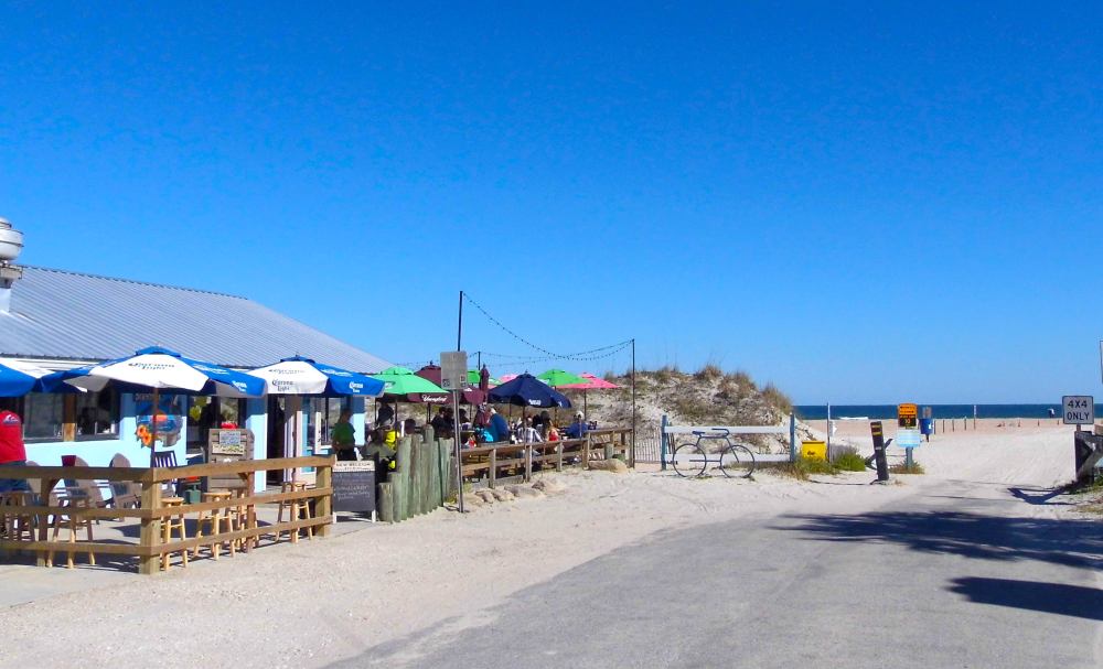 Beachside cafe with colorful umbrellas near sandy path to ocean.