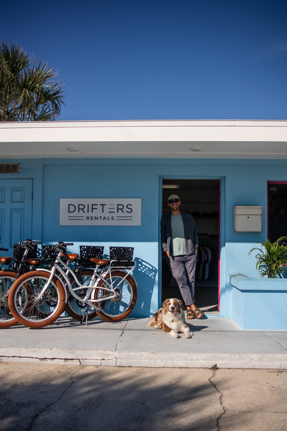Person and dog in front of blue building with 'Drifters Rentals' sign and bicycles.