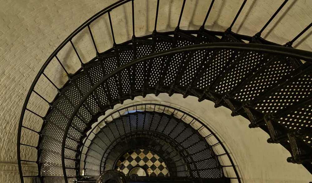 Spiral staircase viewed from above with black metal railing and checkerboard floor at bottom.