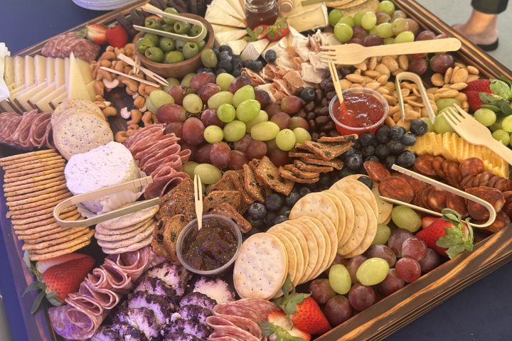 A charcuterie board with meats, cheeses, fruits, nuts, and crackers on a blue tablecloth.