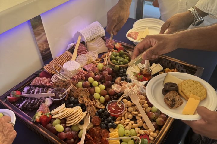 People serving from a charcuterie board with cheese, crackers, fruits, and nuts.