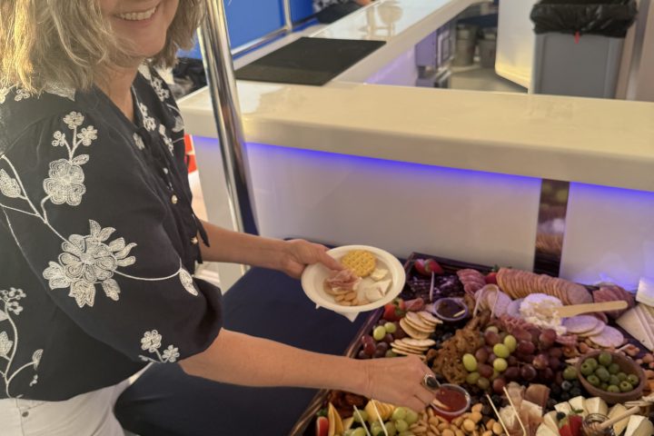 Woman serving from a charcuterie board on a boat with people seated in the background.