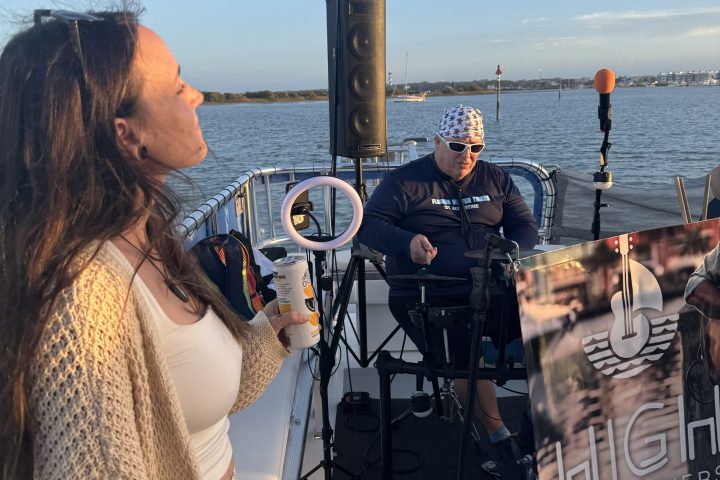 Woman on a boat with a musician playing keyboard, backdrop of water and clear sky.