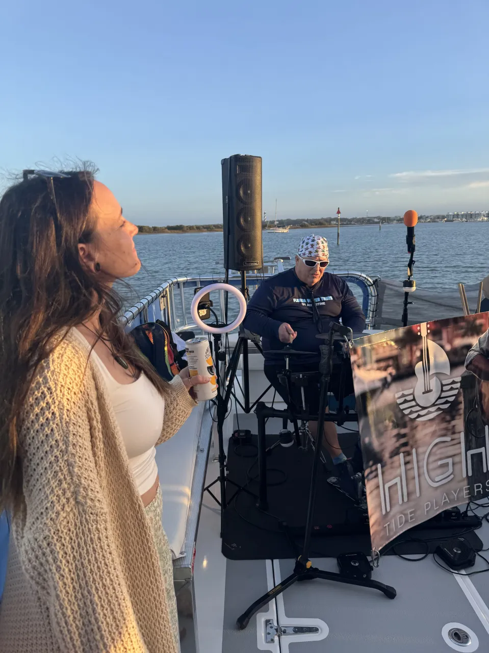 Woman on a boat with a musician playing keyboard, backdrop of water and clear sky.