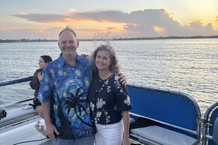 Couple smiling on a boat at sunset with a calm ocean in the background.
