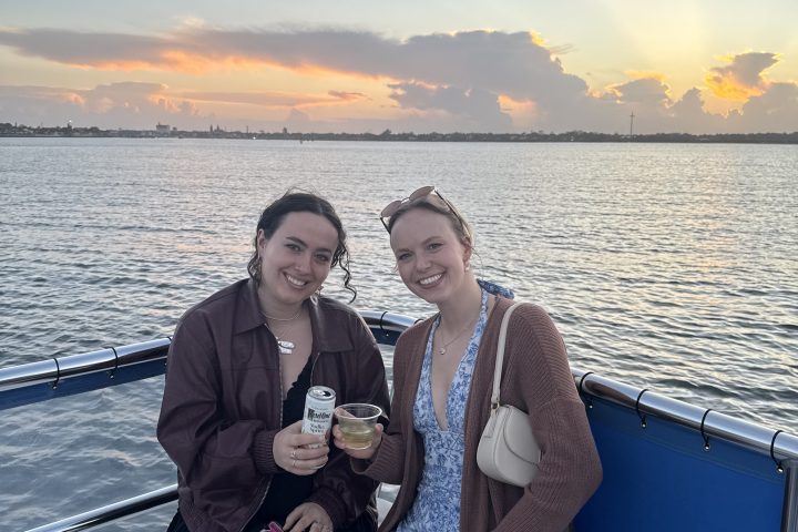 Two people on a boat at sunset holding drinks, with an ocean view.