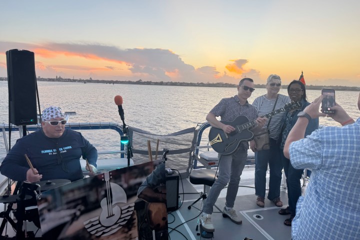 People on a boat enjoy music, with a guitarist playing at sunset.