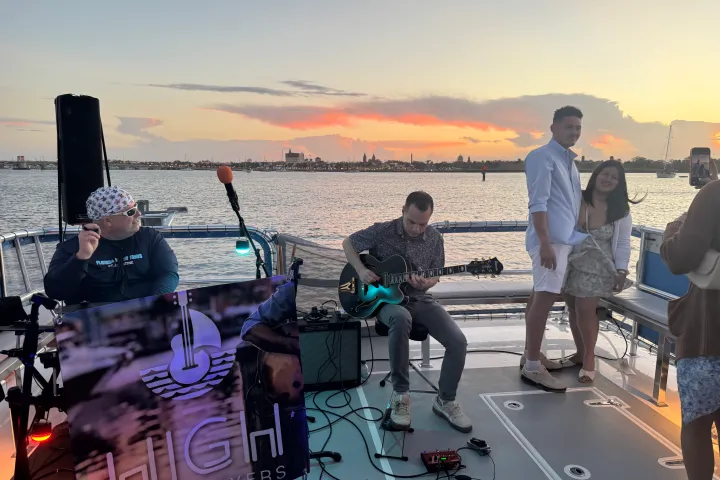 People on a boat at sunset; one plays guitar while others pose for a photo.