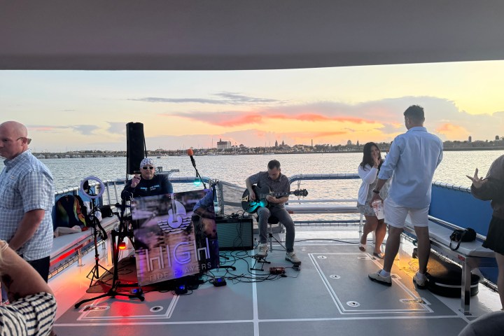 People on a boat at sunset with a band performing and city skyline in the background.