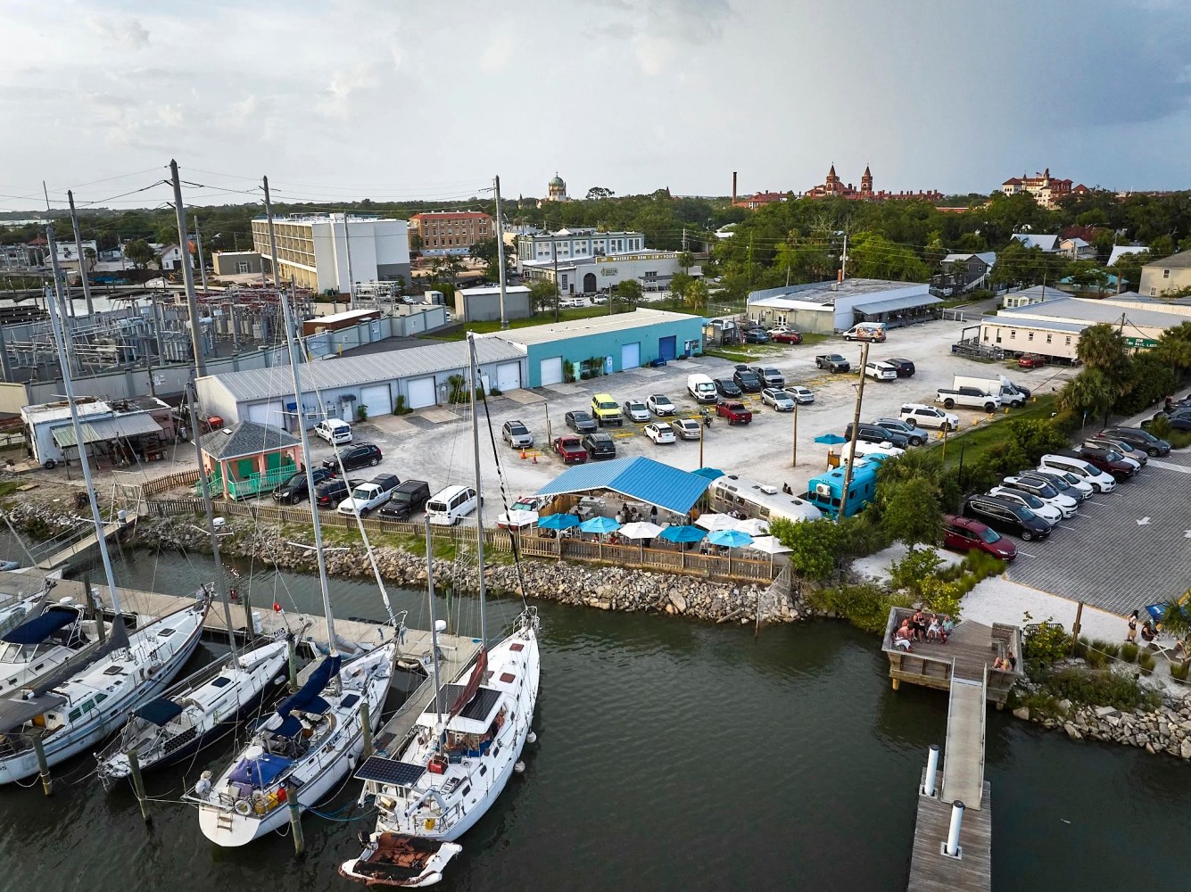 Aerial view of a marina with boats, a parking lot, and buildings in the background.