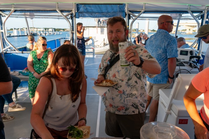 People enjoying a party on a boat, one holding a drink can and plate of food.