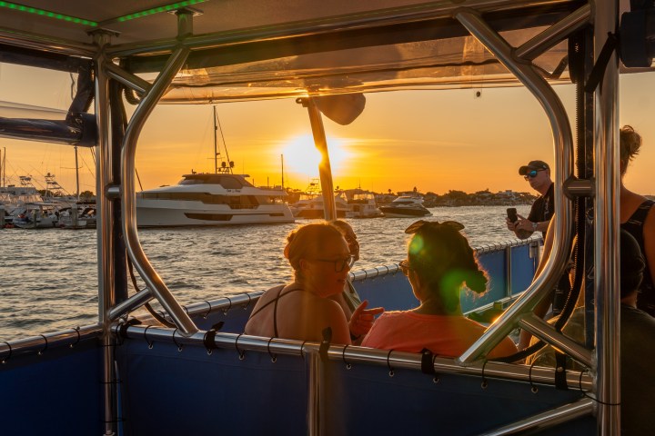 People on a boat at sunset, with yachts visible on the water.