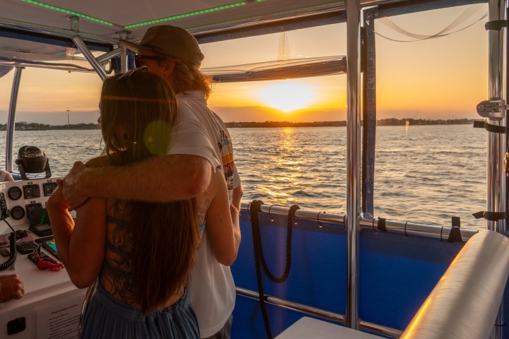 Couple embracing on a boat during sunset, with water view through windows.