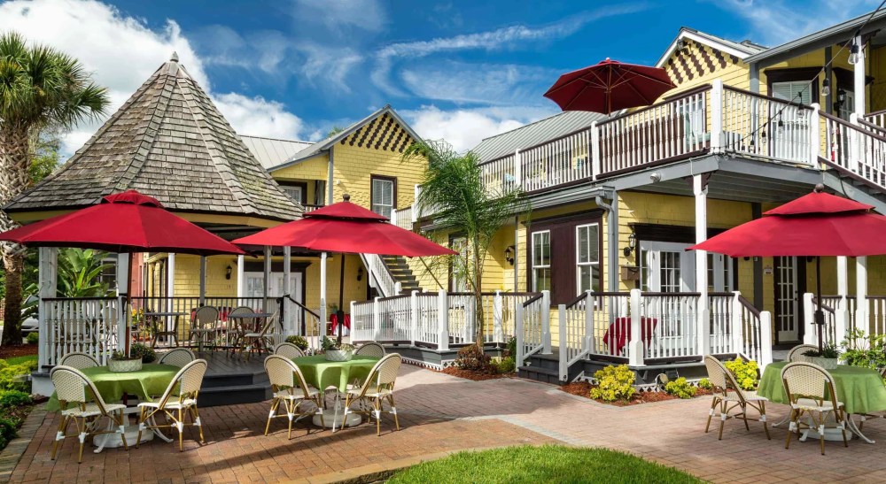 Charming yellow building with outdoor seating under red umbrellas and a blue sky background.