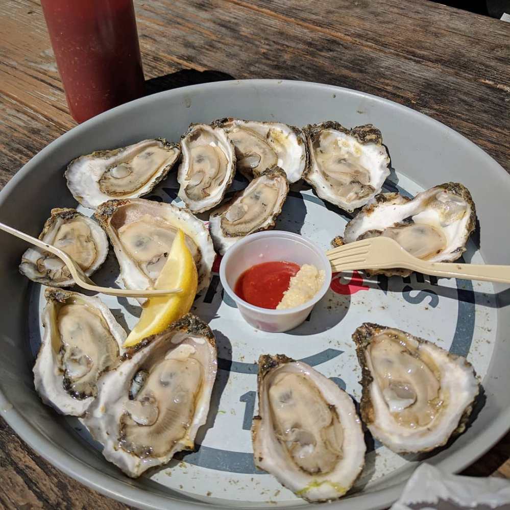 Tray of oysters on the half shell with lemon, sauce, and a wooden fork.