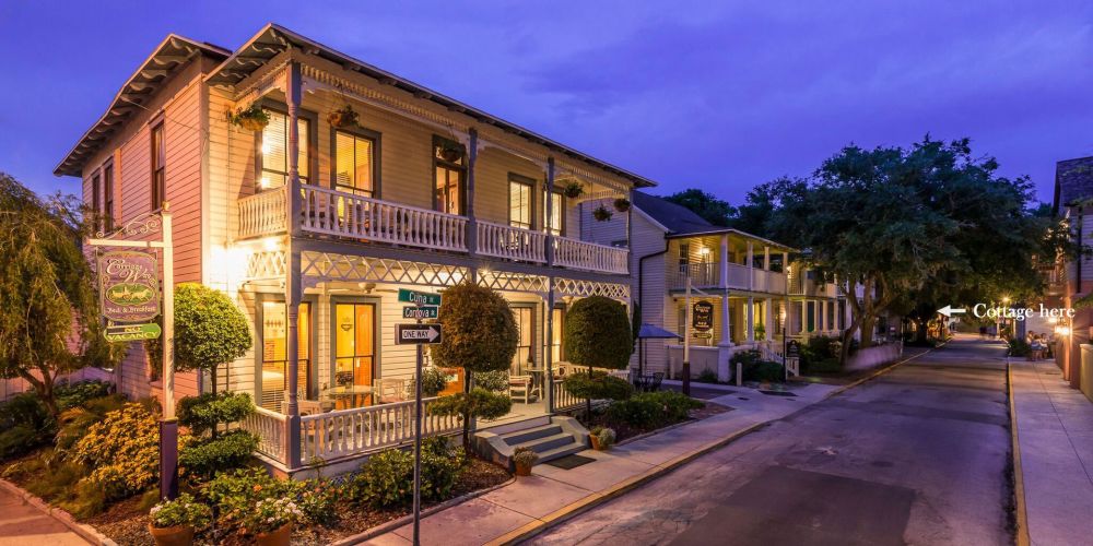 Illuminated two-story bed and breakfast at dusk, with porch and garden, on a quaint street.