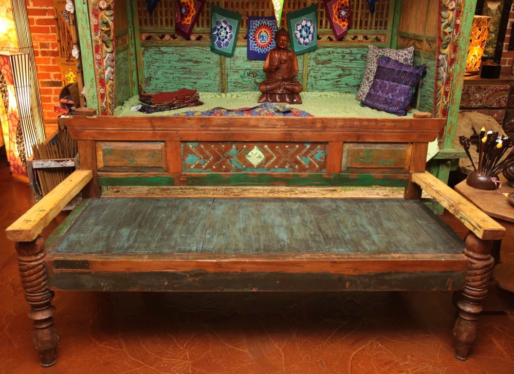 Rustic wooden bench with decorative pillows and a statue on a vibrant backdrop.