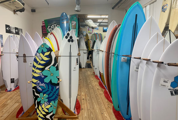 Surfboards displayed in rows inside a shop on wooden floor.