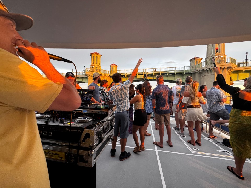 DJ playing music on a boat with people dancing and enjoying the sunset.