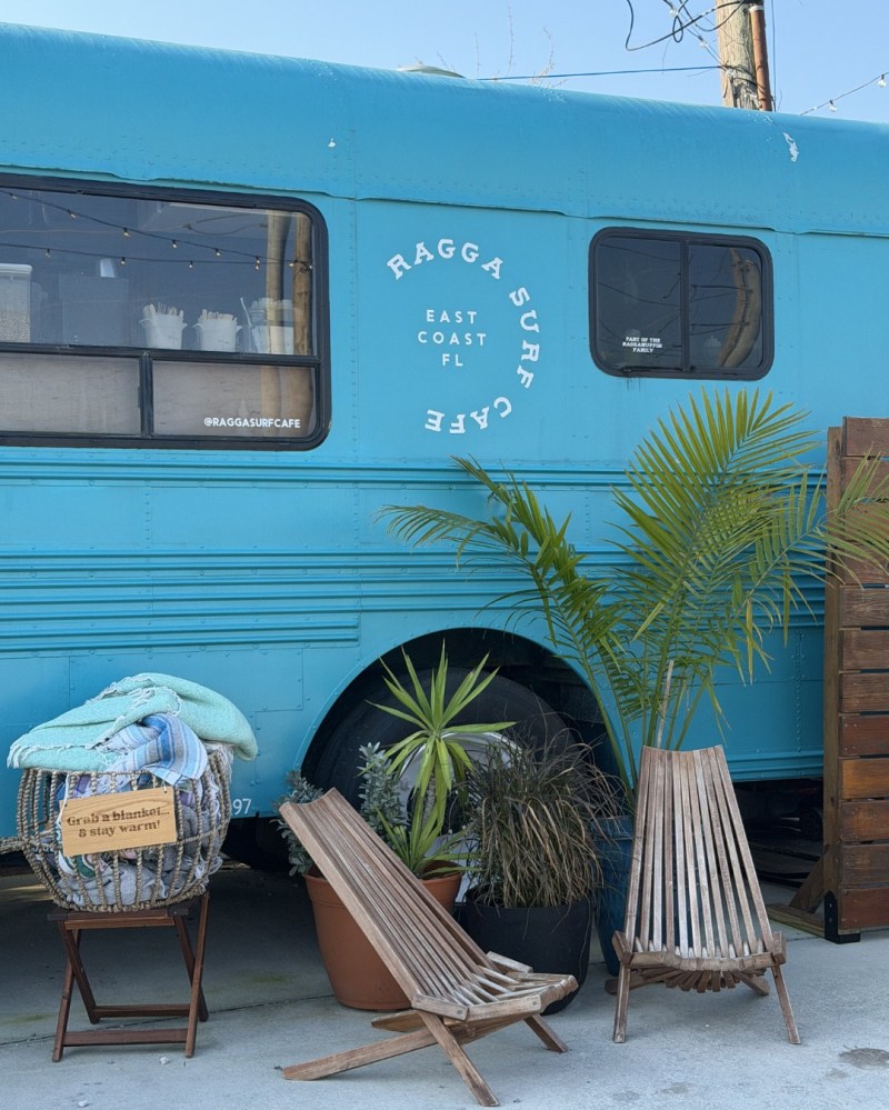 Blue bus café with chairs and plants outside.
