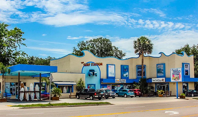 Colorful surf shop with vehicles parked in front under a blue sky.