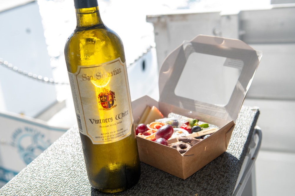 Bottle of wine next to an open food box with assorted snacks.