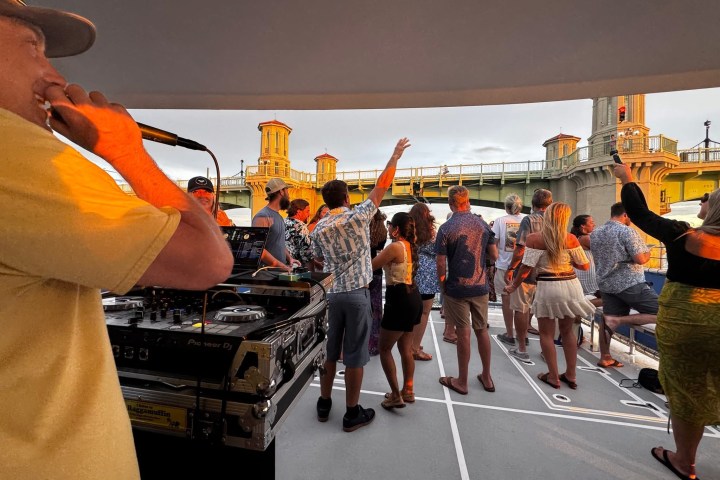 People dancing on a boat with a DJ performing at sunset.