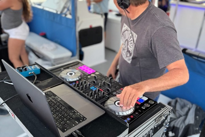 DJ performing on a boat with laptop and mixing equipment, wearing headphones.
